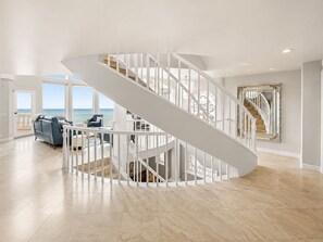 A spacious interior with a white spiral staircase, a seating area with a view of the ocean, and a large mirror on the wall. - Luxury Oceanfront Vacation Home on Hollywood Beach (Oxnard)