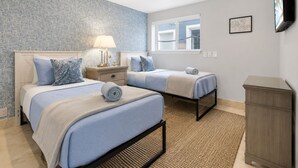 A bedroom with two beds, a nightstand, a lamp, a window, and a TV. - Luxury Oceanfront Vacation Home on Hollywood Beach (Oxnard)