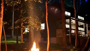 Un feu de camp dans une zone boisée, avec un bâtiment en arrière-plan.