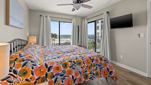 Ein Schlafzimmer mit Bett, Deckenventilator, Fernseher und einem Balkon mit Blick auf den Strand.