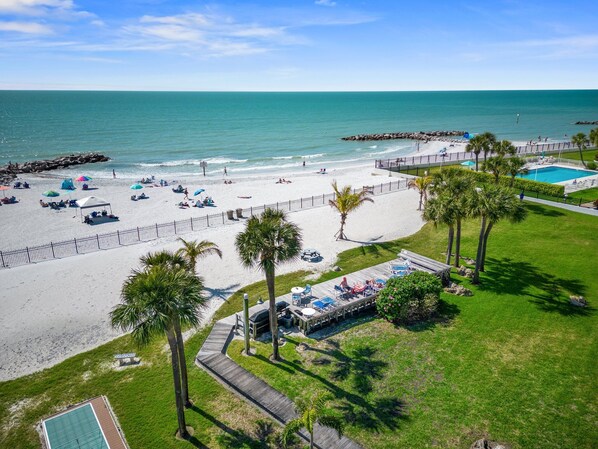 A beach resort with a pool, lounge chairs, and palm trees.