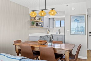 A modern kitchen with light grey cabinets, a wooden dining table, and three hanging pendant lights.