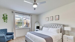 A bedroom with a bed, a chair, a nightstand, a ceiling fan, and a window with blinds. - Spacious Cozy Austin Home with Pool Access (Austin)