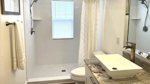Un baño moderno con cabina de ducha, inodoro y lavabo con encimera de mármol.