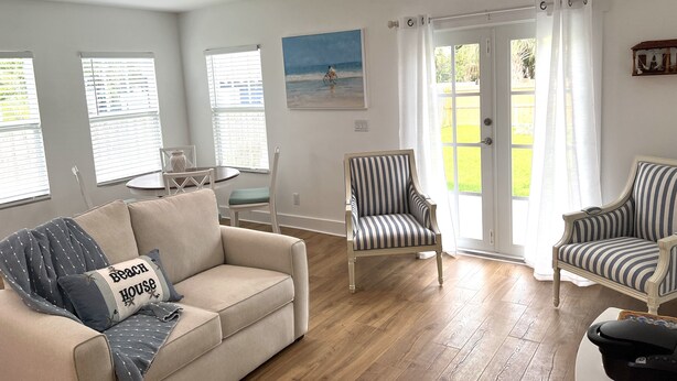 Una sala de estar con un sofá color beige, sillones a rayas, una mesita y un cuadro con una escena de playa.