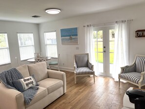Una sala de estar con un sofá color beige, sillones a rayas, una mesita y un cuadro con una escena de playa.