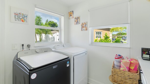 A laundry room with two washing machines, a dryer, and a window with a view of greenery. - Nova Oasis :- Your private vacation playground (West Palm Beach)