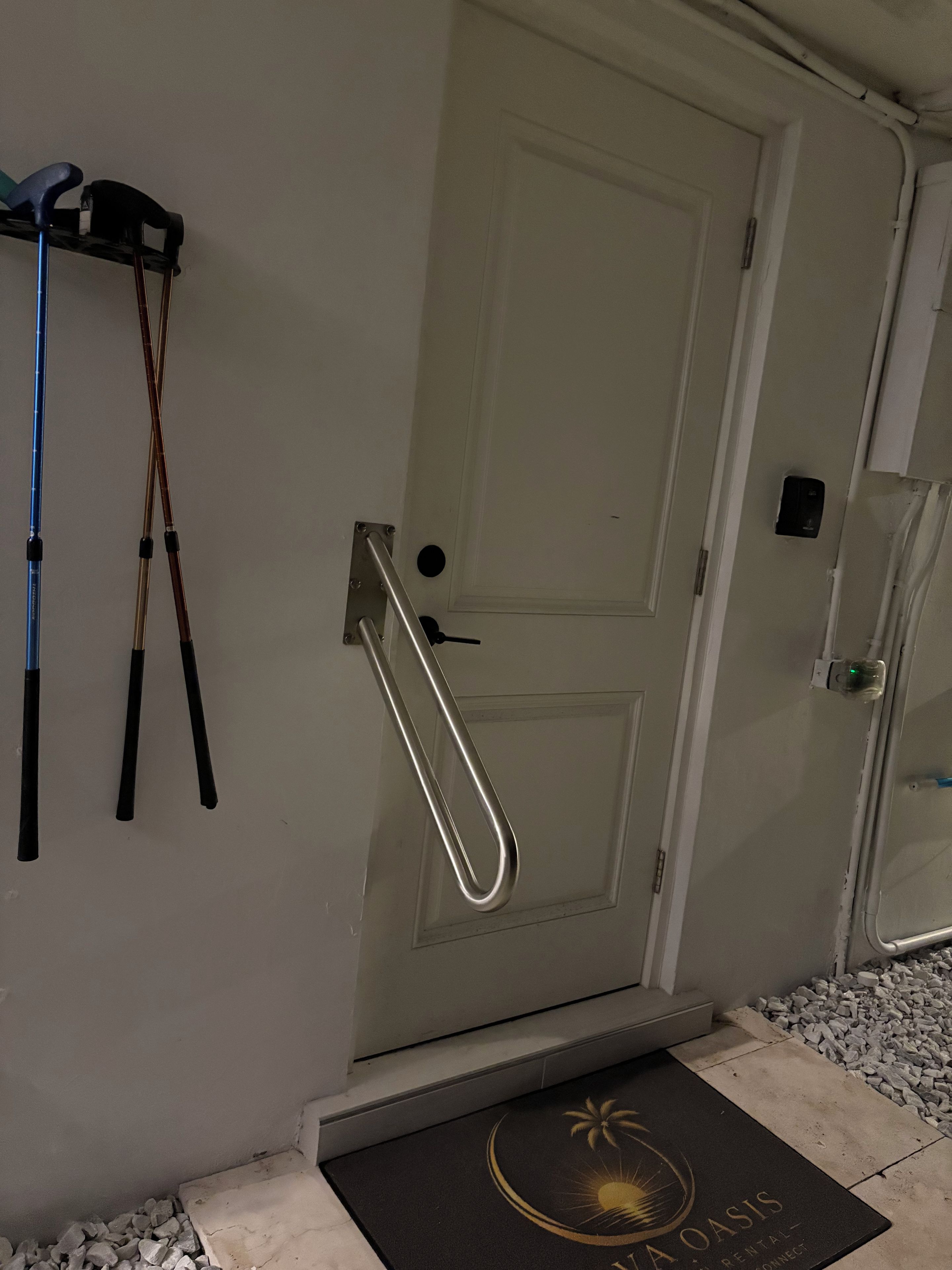 A door with a metal handle and a keyhole, a doormat with a palm tree logo, and a wall-mounted towel rack with towels.
