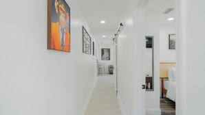 A hallway with artwork on the walls, a door leading to a bedroom, and a small table with a lamp. - Nova Oasis :- Your private vacation playground (West Palm Beach)