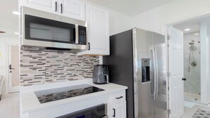 A modern kitchen with white cabinetry, a stainless steel refrigerator, a microwave, and a coffee maker. - Nova Oasis :- Your private vacation playground (West Palm Beach)