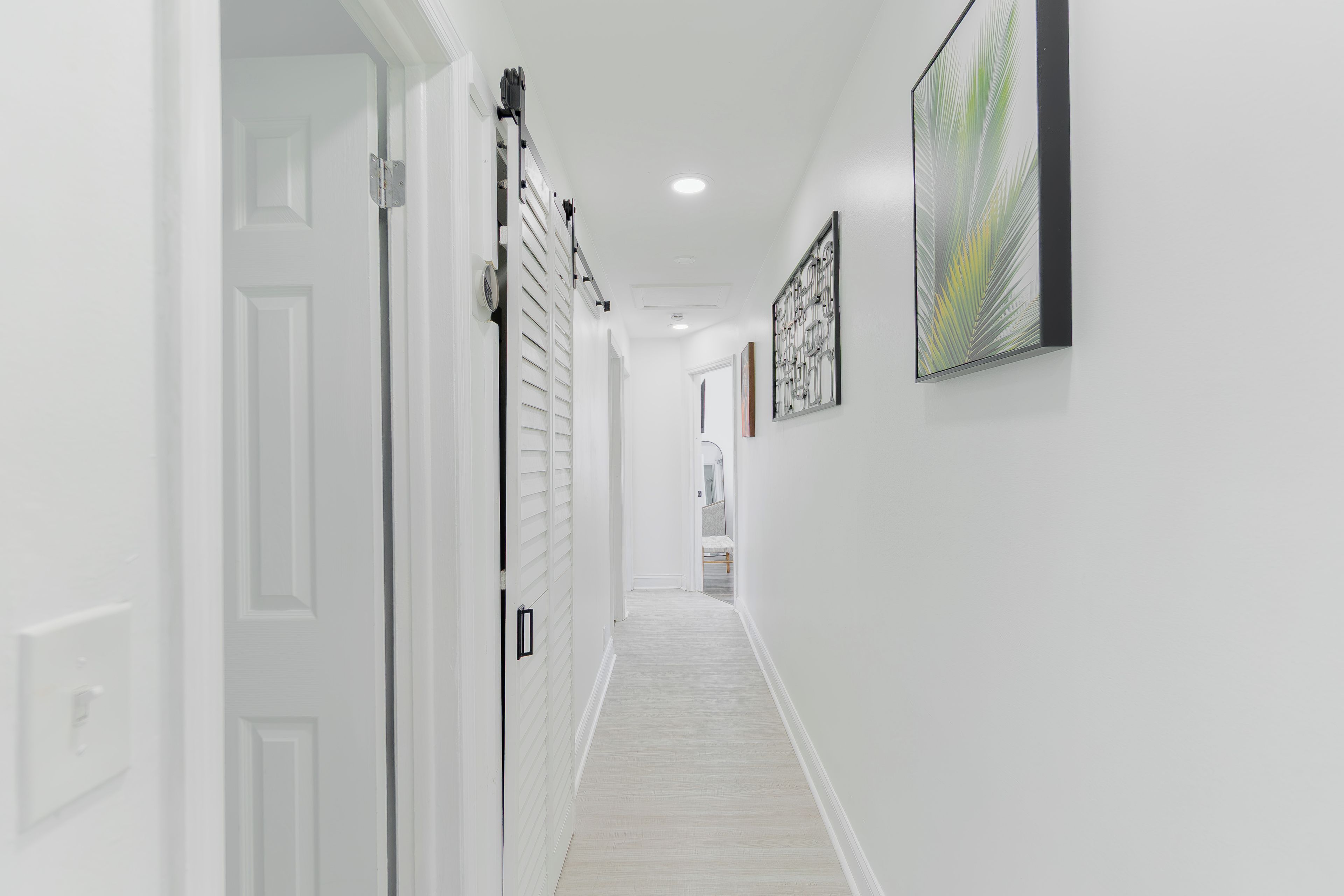 A hallway with white walls, a light-colored floor, and a door with a white frame.