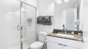 A modern bathroom with a glass shower enclosure, a white toilet, and a vanity with a mirror. - Luxury Downtown DC Apartment - Near City Center (Washington)