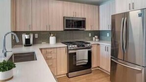 A modern kitchen with light wood cabinets, stainless steel appliances, and a central island with a sink and countertop. - Luxury Downtown DC Apartment - Near City Center (Washington)