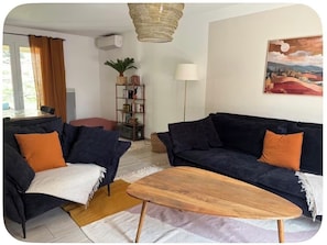 A living room with a dark blue sofa, a wooden coffee table, a bookshelf, a lamp, and a painting on the wall.