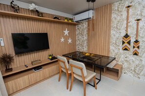 A modern dining area with a wooden panel wall, a flat-screen TV, a glass dining table, and two wooden chairs. - Flamboyant Caribessa (João Pessoa)