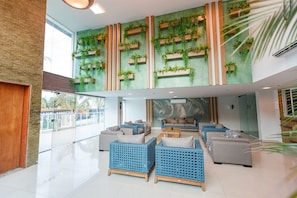 Um lobby amplo com teto alto, área de estar com sofás azul e cinza, e parede verde com jardins verticais.