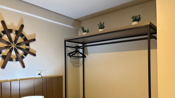 A room with a wooden floor, a wall-mounted coat rack, a shelf with towels, a lamp, and a decorative wall piece. - Flamboyant Caribessa (João Pessoa)