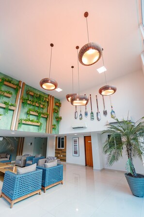 A lobby with wicker ceiling lamps, a wall-mounted plant display, and blue wicker sofas.