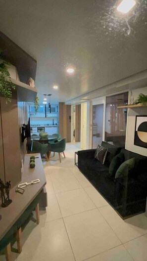 A modern living room with a black sofa, a dining area with a green table, and a kitchen in the background. - Flamboyant Caribessa (João Pessoa)