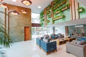 A spacious lobby with wicker sofas, a wooden coffee table, and a green wall with plants. - Flamboyant Caribessa (João Pessoa)