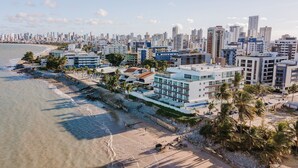 A coastal cityscape with modern buildings, a beach, and palm trees. - Flamboyant Caribessa (João Pessoa)