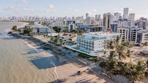 Paisagem costeira com edifícios modernos, uma praia e palmeiras.