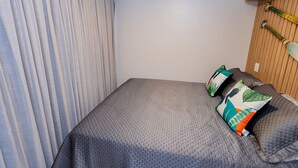 A neatly made bed with a grey quilt, a wooden headboard, and a shelf with decorative items. - Flamboyant Caribessa (João Pessoa)
