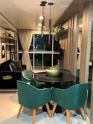 A modern dining area with a round table, teal chairs, and pendant lighting.
