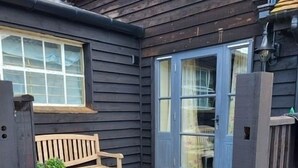 A wooden deck with a stone-tiled patio, a wooden bench, and a blue door. - The Old Dairy, 200 years old and newly converted (Barcombe)