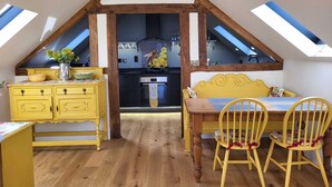 A cozy attic room with a wooden ceiling, a dining table with yellow chairs, and a yellow dresser. - The Old Dairy, 200 years old and newly converted (Barcombe)