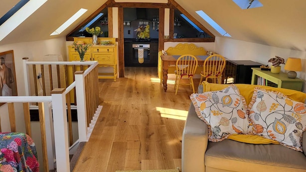 A cozy attic room with a wooden staircase, a dining area with yellow chairs, and a sofa with patterned cushions. - The Old Dairy, 200 years old and newly converted (Barcombe)