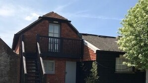 A two-story house with a balcony, a front door, and a staircase leading to the entrance. - The Old Dairy, 200 years old and newly converted (Barcombe)