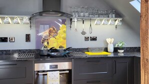 A modern kitchen with dark cabinetry, a stainless steel range hood, and a variety of kitchen utensils and glassware on the wall. - The Old Dairy, 200 years old and newly converted (Barcombe)