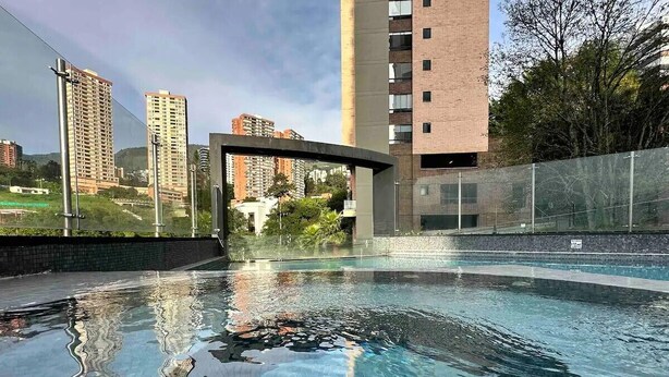 Ein Schwimmbecken mit klarem Wasser, umgeben von einem Zaun und Gebäuden im Hintergrund.