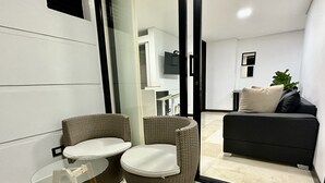 Ein modernes Wohnzimmer mit einem Glastisch, zwei Korbstühlen, einem schwarzen Sofa und einem großen Spiegel, der den Raum reflektiert.