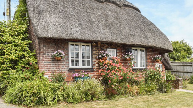 A traditional thatched-roof cottage with brick walls, two windows with white frames, and flower boxes on the windowsills. - 2 bedroom accommodation in Hailsham (Hailsham)