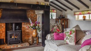 A cozy living room with a fireplace, a sofa with floral cushions, and a vase of flowers. - 2 bedroom accommodation in Hailsham (Hailsham)