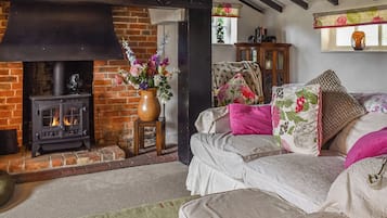 A cozy living room with a fireplace, a sofa with floral cushions, and a vase of flowers.
