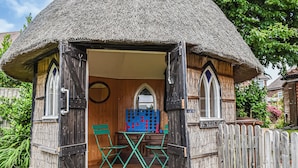 A rustic wooden structure with a thatched roof, a wooden door, and a small table with chairs inside. - 2 bedroom accommodation in Hailsham (Hailsham)