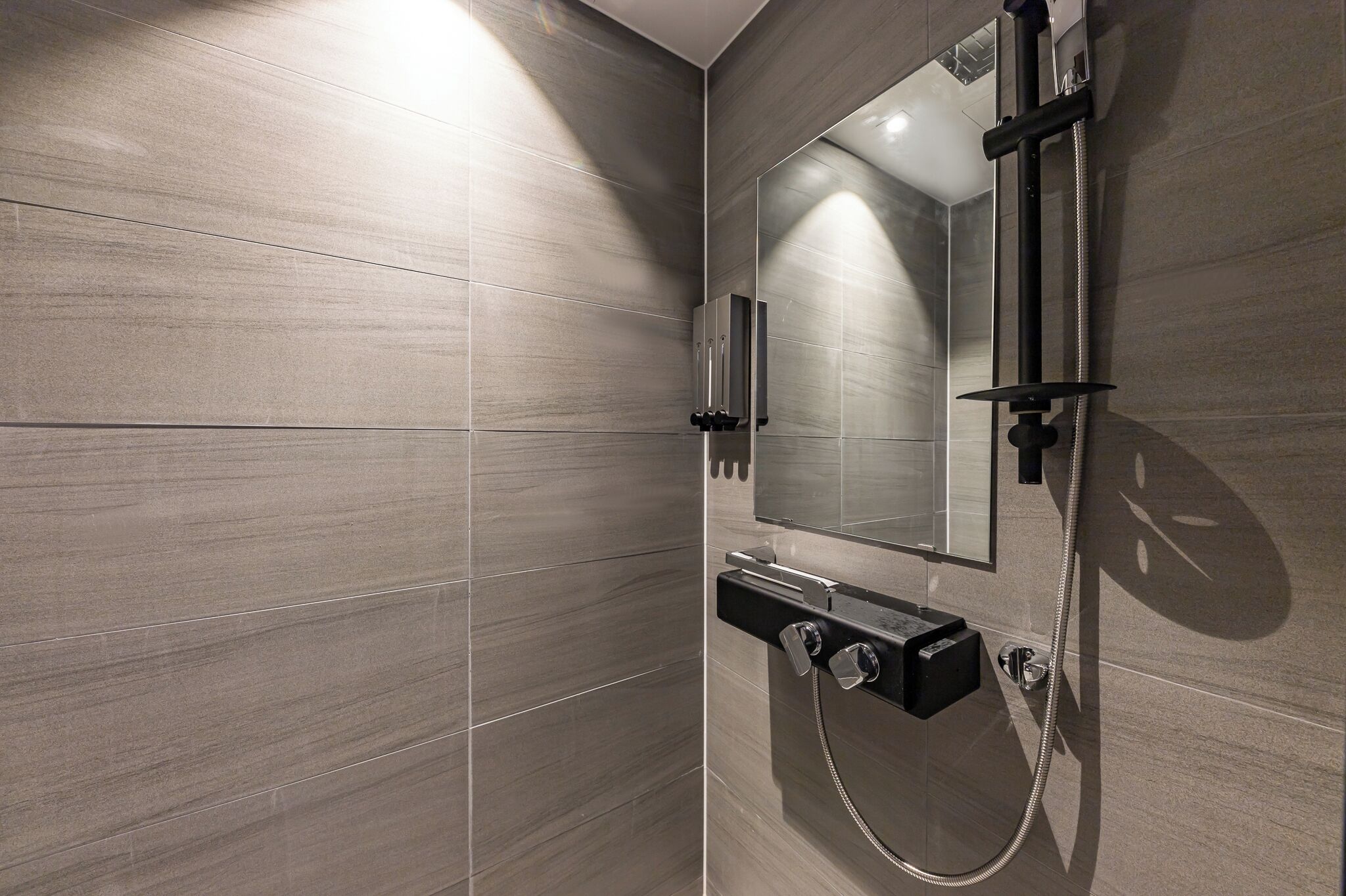 Une douche moderne dotée d’un pommeau de douche à main et d’un panneau de commande fixé au mur.