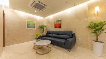 A modern lobby with a grey sofa, a round coffee table, and two potted plants.