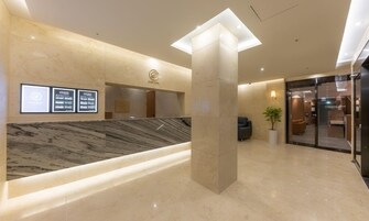 Zona de recepción de un hotel con un mostrador de mármol, un pilar grande y una puerta de cristal que da a un vestíbulo con asientos.