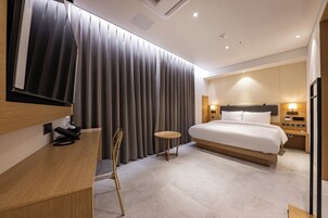 Una habitación de hotel moderna con una cama grande, un escritorio con teléfono, una mesita redonda y un separador de cortinas.