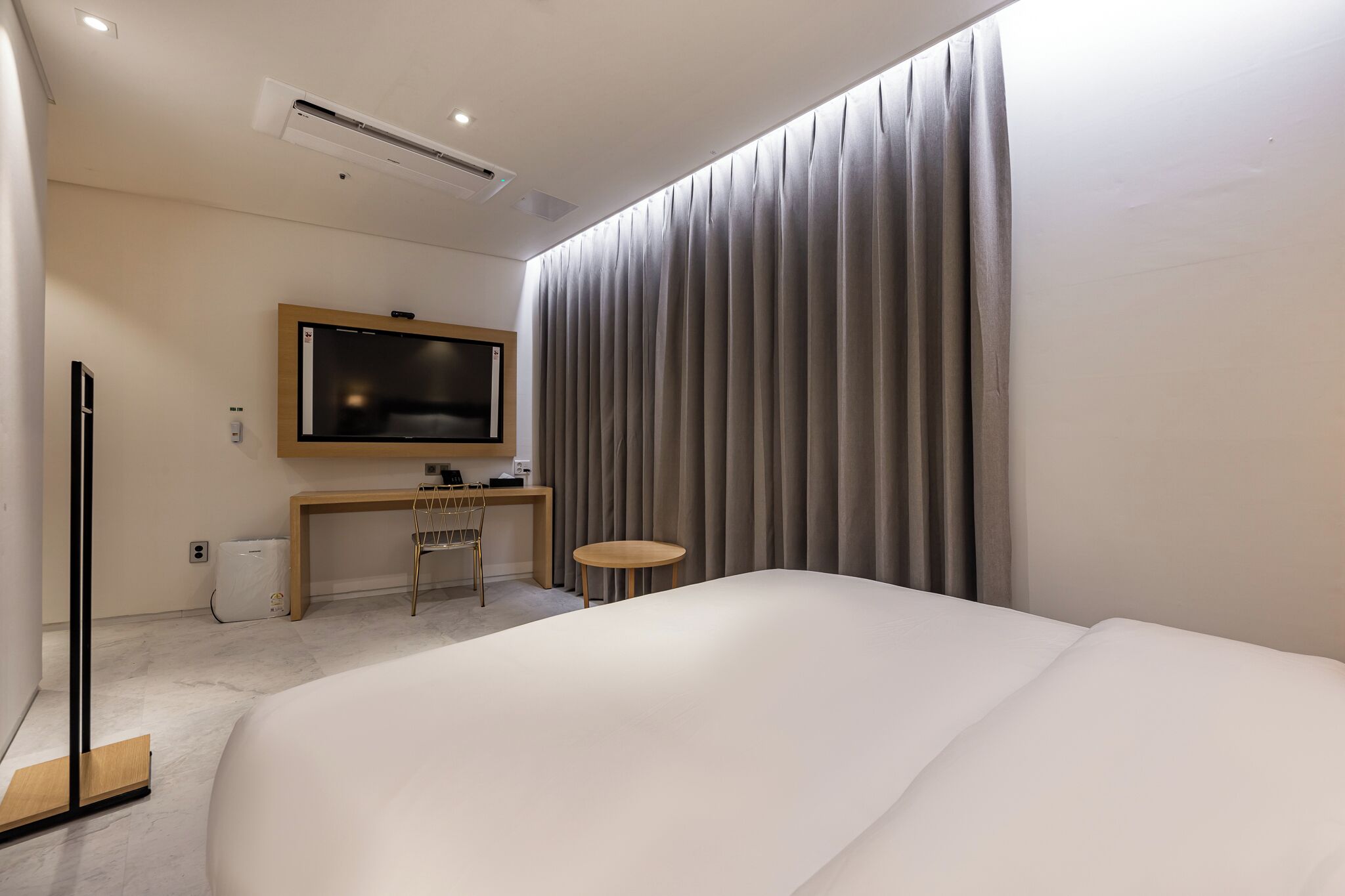 A modern hotel room with a large bed, a desk with a flat-screen TV, a chair, and a small round table.