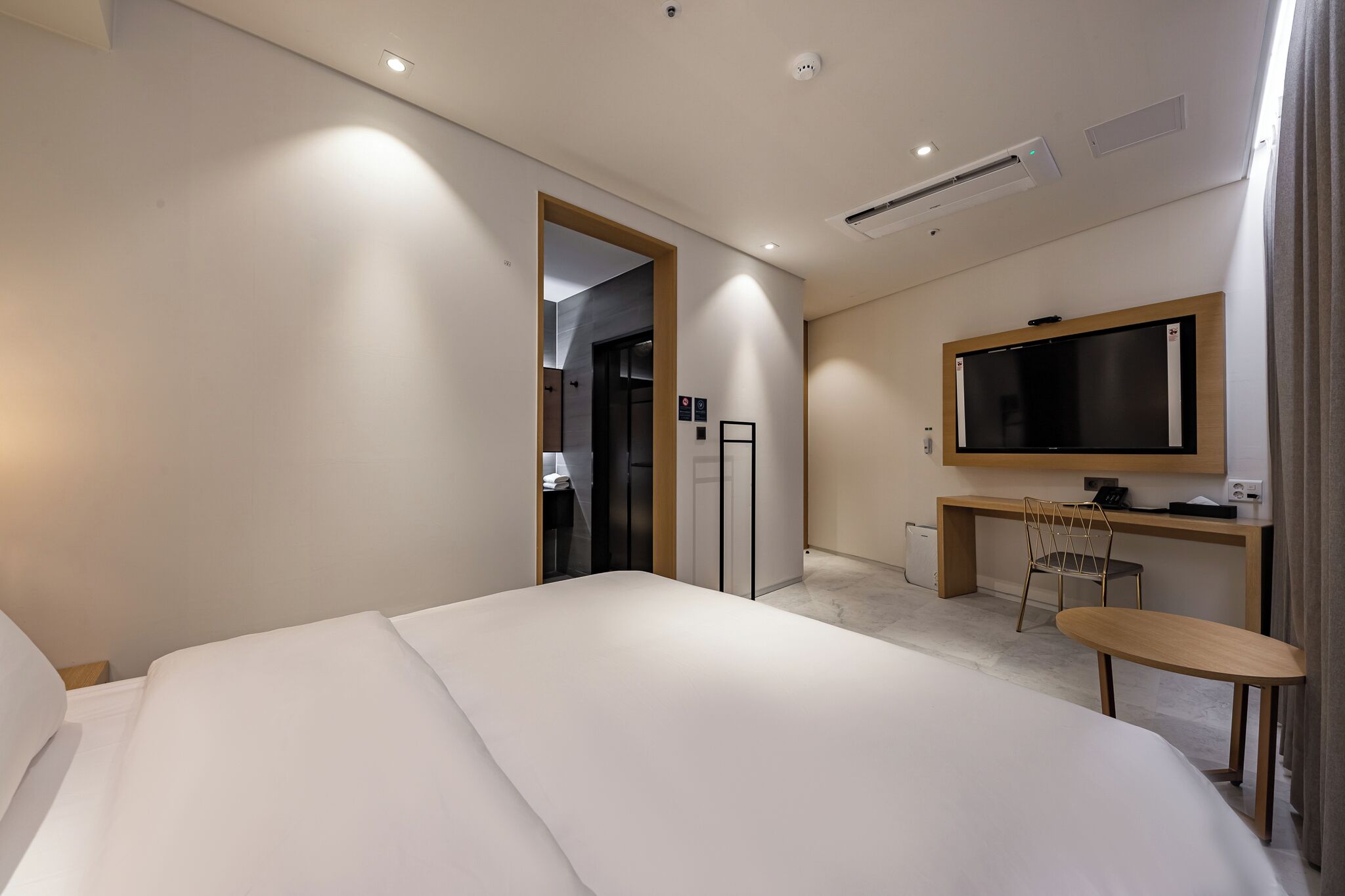 A modern hotel room with a large bed, a desk with a chair, a television, and a wardrobe.