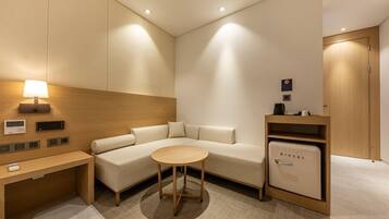 Una habitación de hotel moderna con sofá, una mesita redonda, minibar y lámpara.