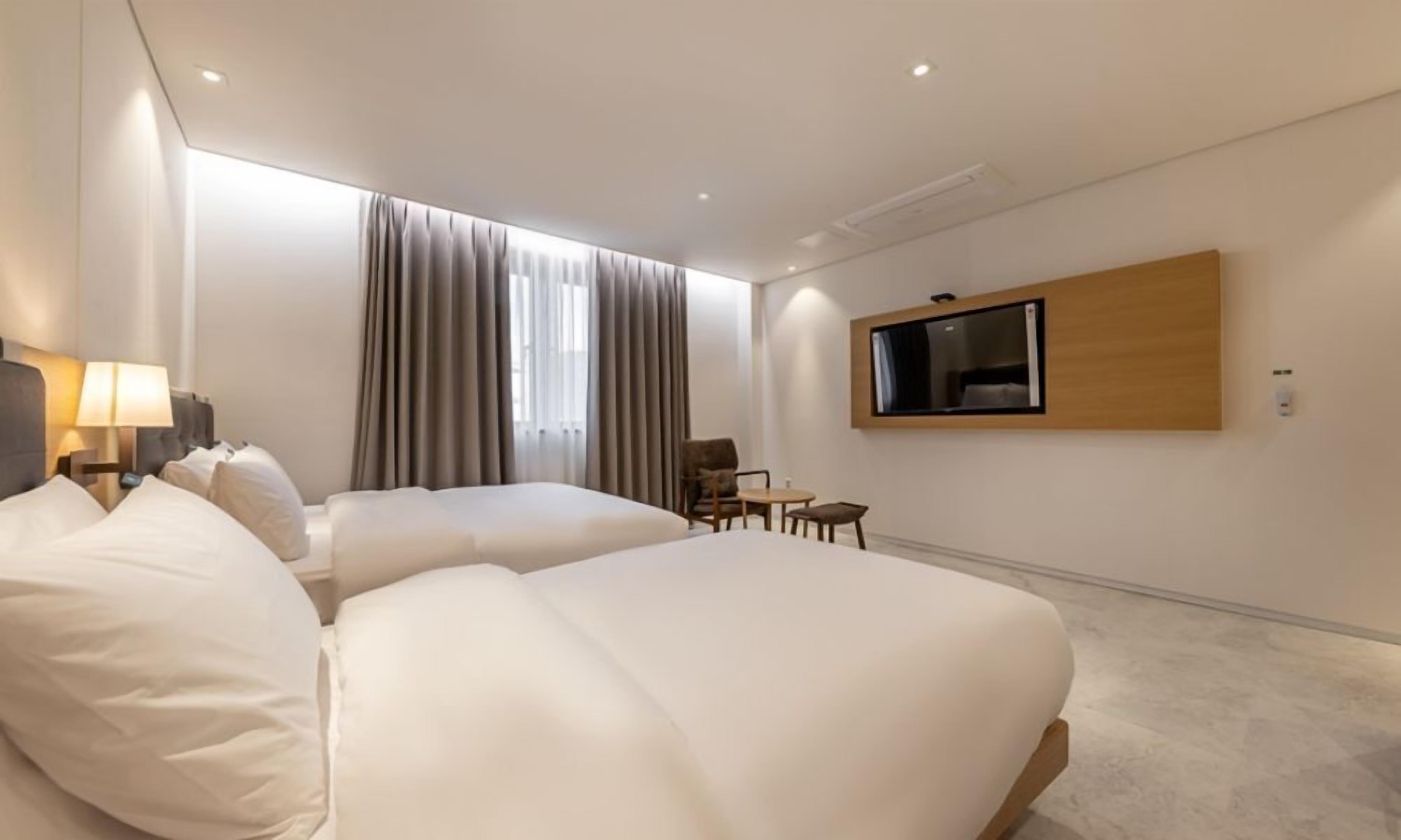 A hotel room with two beds, a TV mounted on the wall, a desk, and a chair.