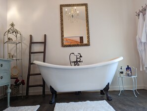 Ein Badezimmer mit einer freistehenden Badewanne, einer Holzleiter, einem Waschtisch mit Spiegel und einer Pendelleuchte.
