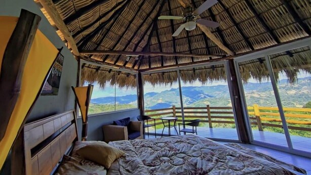 Un dormitorio con una cama grande, un ventilador de techo y vistas a las montañas a través de amplios ventanales.