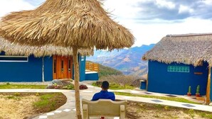 A person sitting under a thatched roof structure in a courtyard with a mountain view.